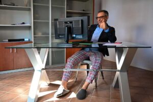 Uomo che lavora dalla scrivania di casa, con giacca e camicia sopra, ma ciabatte e pigiama sotto