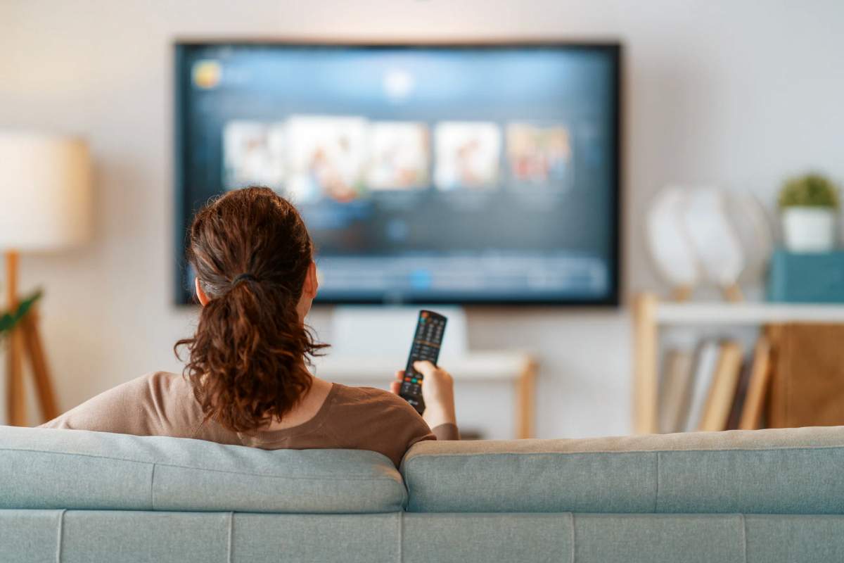 Donna seduta davanti alla TV accesa con telecomando in mano