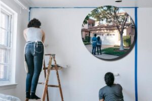 Due giovani intenti a ridipingere una parete e in evidenza una coppia di fronte a una casa nuova